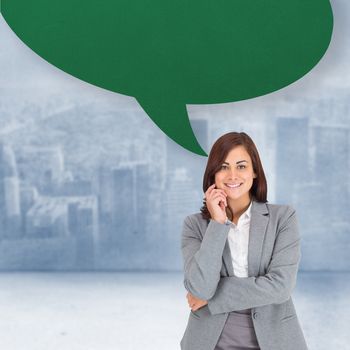 Smiling thoughtful businesswoman with speech bubble against city scene in a room