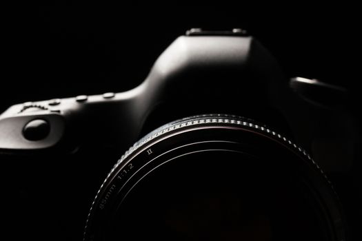 Professional modern DSLR camera low key image - Modern DSLR camera with a very wide aperture lens on