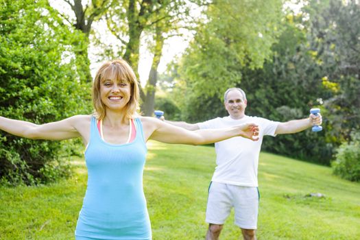 Female fitness instructor exercising with middle aged man outdoors in summer park