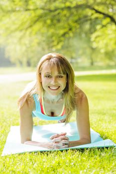 Female fitness instructor holding plank pose exercising outside in green summer park