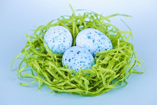 Three blue speckled easter eggs in green paper grass nest