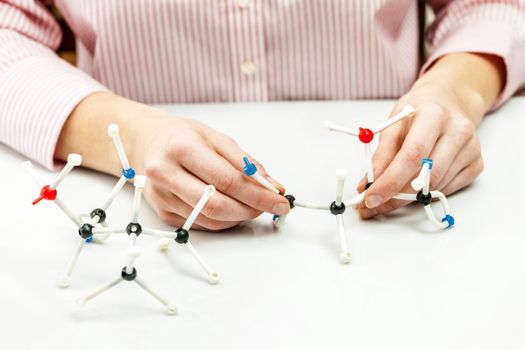 Hand of female student assembling amino acid molecule models for science project