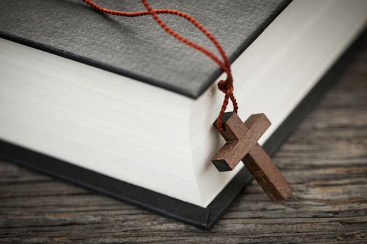 Closeup of wooden Christian cross necklace next to holy Bible