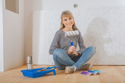 happy smiling female painter sitting on wooden floor and holding paintroller