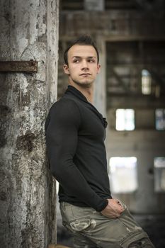 Good looking young man in abandoned warehouse standing against concrete column