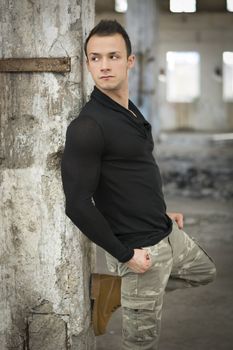 Good looking young man in abandoned warehouse standing against concrete column