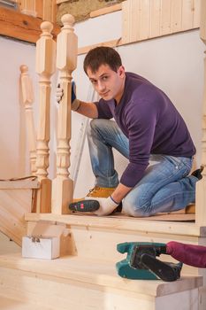 young worker fixing post of wooden  ladder and looking at camera
