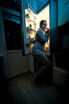 Photo of hungry woman eating at night near refrigerator