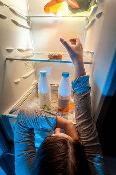 Young woman taking donut from top shelf of refrigerator
