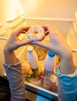 Closeup photo of hands taking big donut from top shelf of fridge