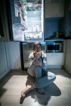 Beautiful woman sitting near refrigerator at late night