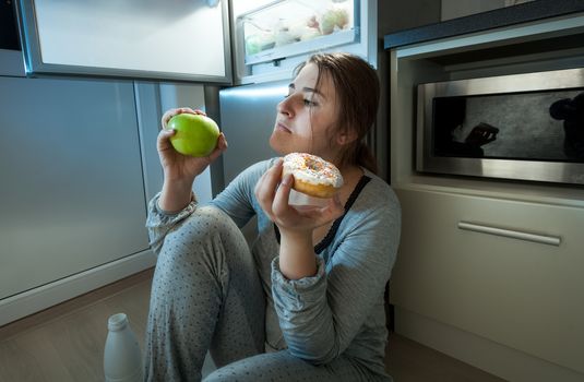 Closeup portrait of woman choosing between apple and donut at evening lunch