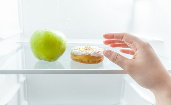 Closeup portrait of hand choosing between apple and donut at fridge