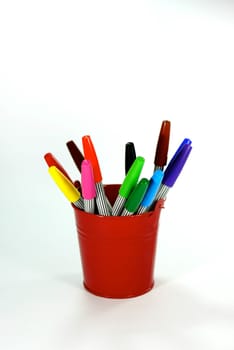 Add a description…various colours of magic pen in red bucket on white scene,shallow focus