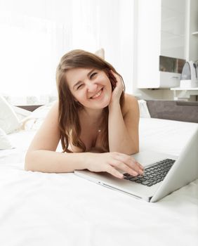 Closeup portrait of cute smiling woman lying in bed with laptop