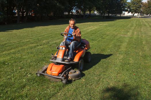 Man with ride-on lawn mower cutting grass.