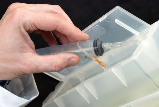 Close-up of a syringe with butterfly needle being dropped into sharps container.