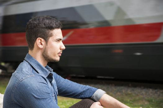 Profile view of young man sitting in front of moving train, serious expression