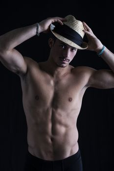Shirtless young latino man with straw hat on dark background