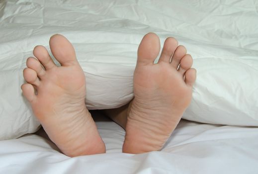 Foot rests on a bed covered with a white cloth.