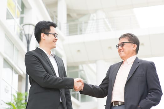 Asian businessmen handshaking. Senior CEO hand shake with young executive. Modern  office building architecture background.