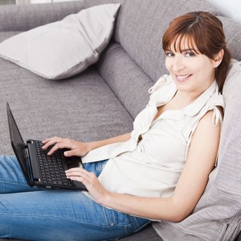 Beautiful woman at home seated on sofa and working with a laptop