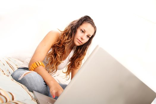 A young girl sitting on the bed and surfing on the Internet with a Laptop. Isolated on white.