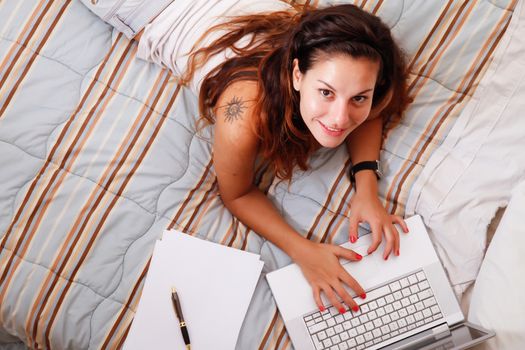 A young adult girl studying on the bed with a Laptop.