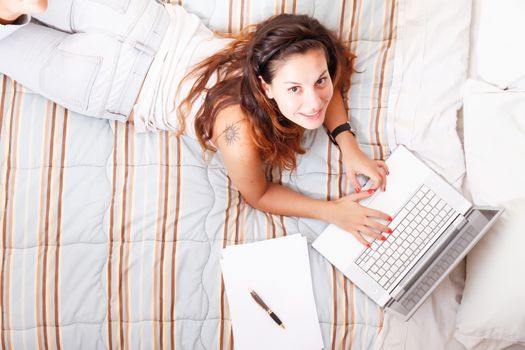 A young adult girl studying on the bed with a Laptop.