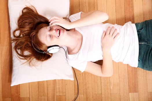 A young redhead girl lying on the floor while listening music.