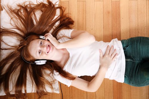 A young redhead girl lying on the floor while listening music.
