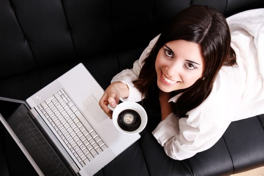 A young, hispanic adult girl watching a Laptop while drinking coffee.