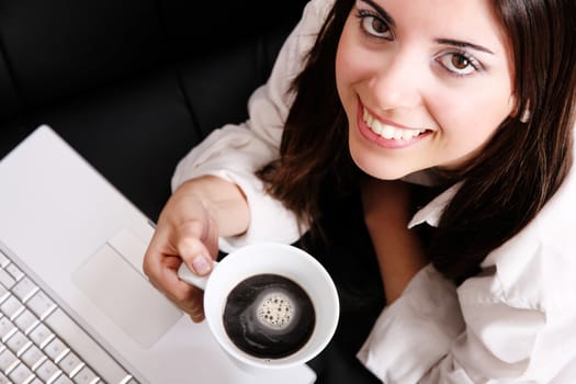 A young, hispanic adult girl watching a Laptop while drinking coffee.