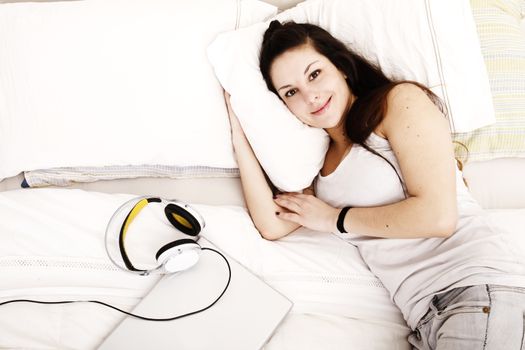 A young adult Woman relaxing on the Bed with a Laptop and Headphones..