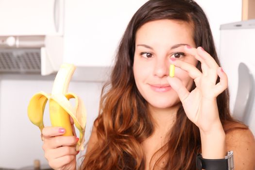 A young woman holding a supplement pill in one hand and a banana in the other.