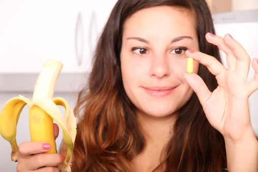 A young woman holding a supplement pill in one hand and a banana in the other.