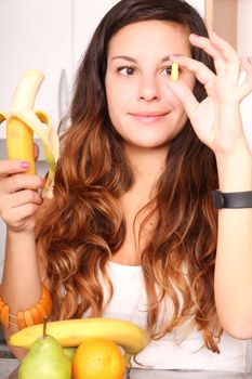 A young woman holding a supplement pill in one hand and a banana in the other.