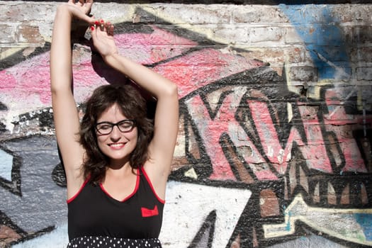 A vintage style dressed girl leaning at a graffiti wall and enjoying the sunlight.