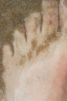 Bare feet under water, covered with sand