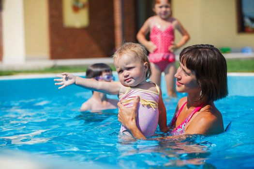 Summer vacations concept. Happy mother and daughter playing in blue water of swimming pool.