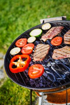 Barbecue on a hot day during the summer vacation on a green grass background. Meat and vegetables on the grill.