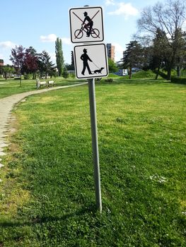 Entrance to a park with sign pole saying that pets are allowed but bicycling is not