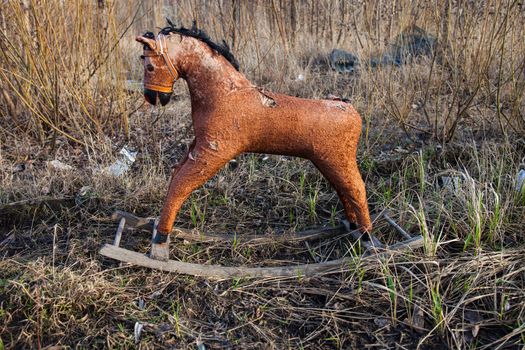 Old threadbare rocking horse thrown away to the dump in the field