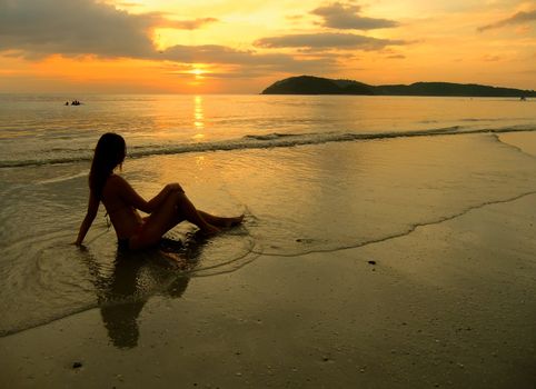Young woman in bikini sitting on a beach at sunset, Langkawi island, Malaysia, Southeast Asia