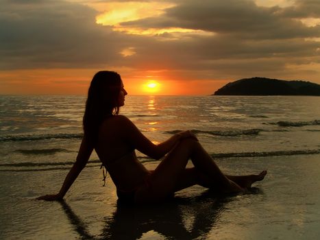 Young woman in bikini sitting on a beach at sunset, Langkawi island, Malaysia, Southeast Asia