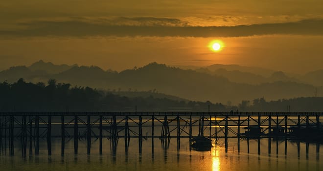 The sun's rising in the morning behind the wooden bridge.