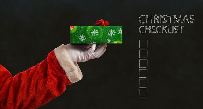 Santa Claus Father Christmas hand with wrapping paper present on blackboard checklist background