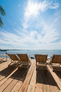 Vacation Concept. Relaxing sunbeds on wooden desk near the sea under blue sky.