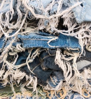 Heap of blue jeans denim torn tear thread along the edges background
