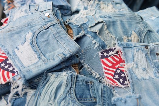 Heap of torn and frayed, threadbare jeans denim shorts with bright pockets with flag elements